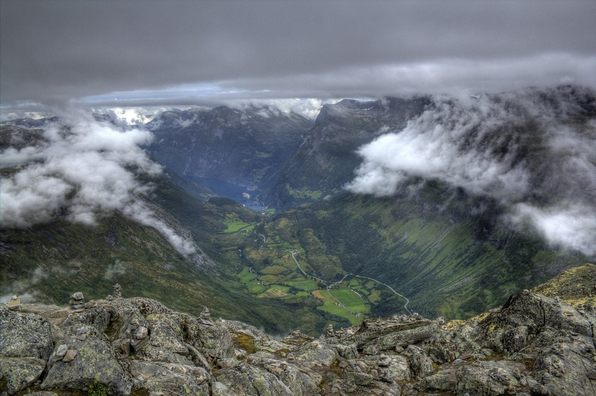 Utsikt från Dalsnibba ner mot Geirangerfjorden och byn Geiranger mellan branta fjällsidor och moln